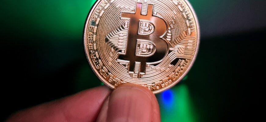 a hand holding a bit coin in front of a green light