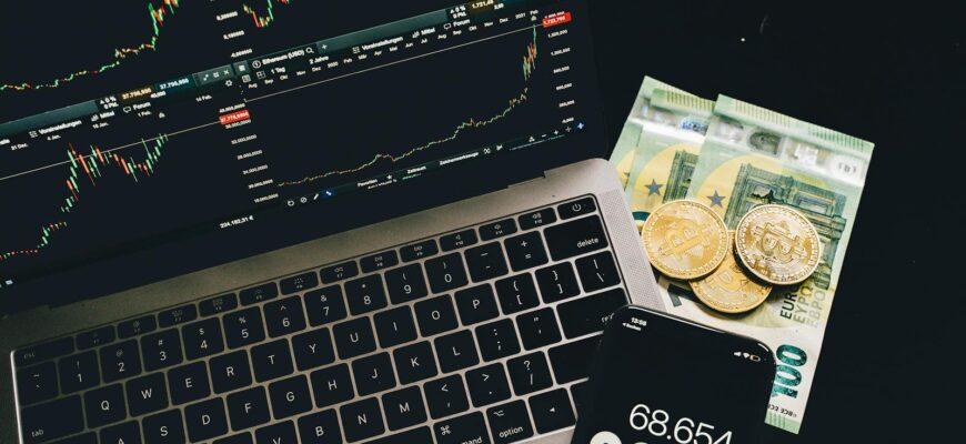 A laptop displaying stock charts with Bitcoin, Euros, and a cellphone calculator, showcasing financial analysis.